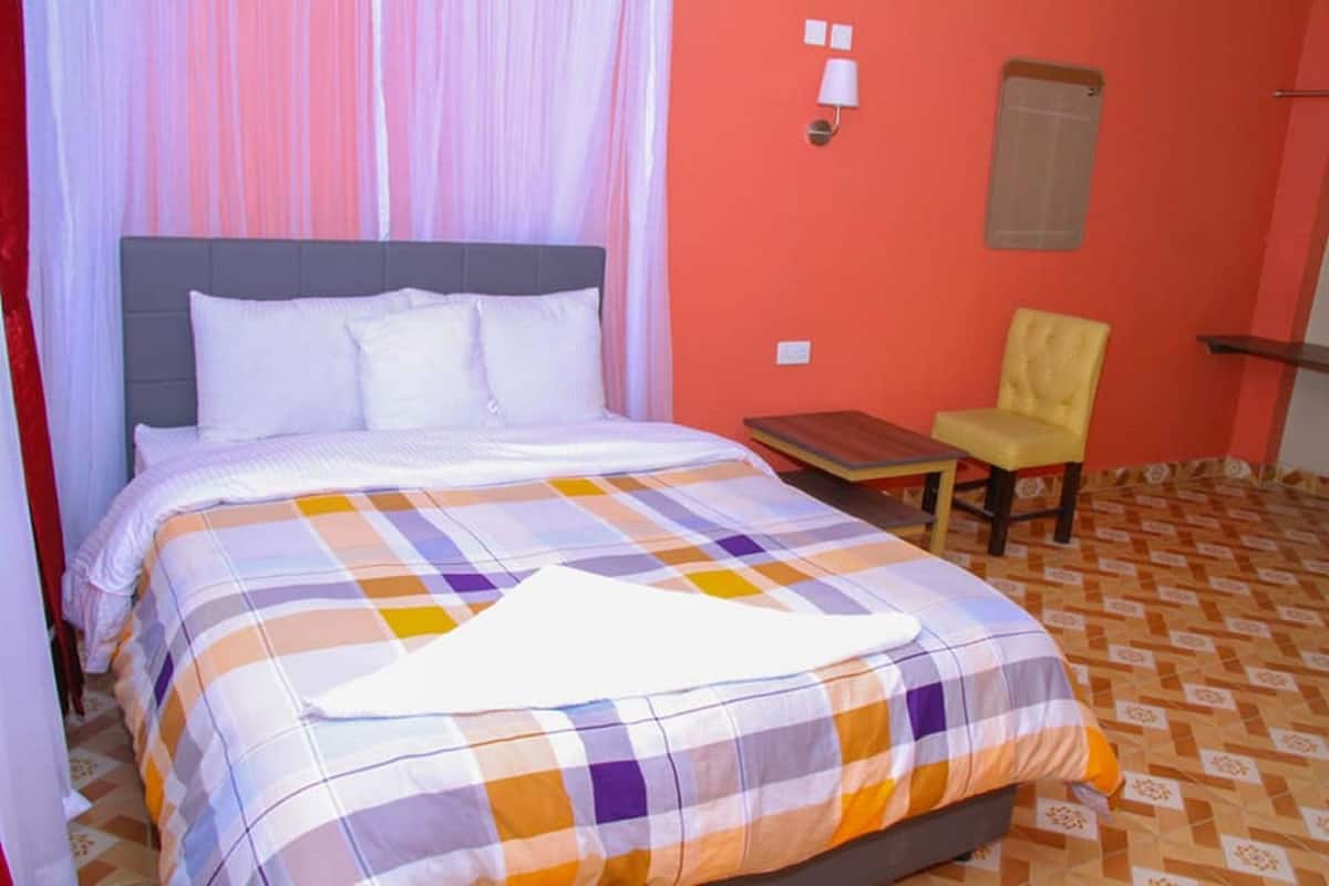 A bed with a checkered bedspread, a bedside table, a chair, and a wall-mounted lamp.