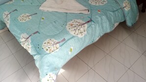 A bed with a floral-patterned bedspread and pillows, a wooden headboard, and a tiled floor. - Njiwa Guest House (Nakuru)