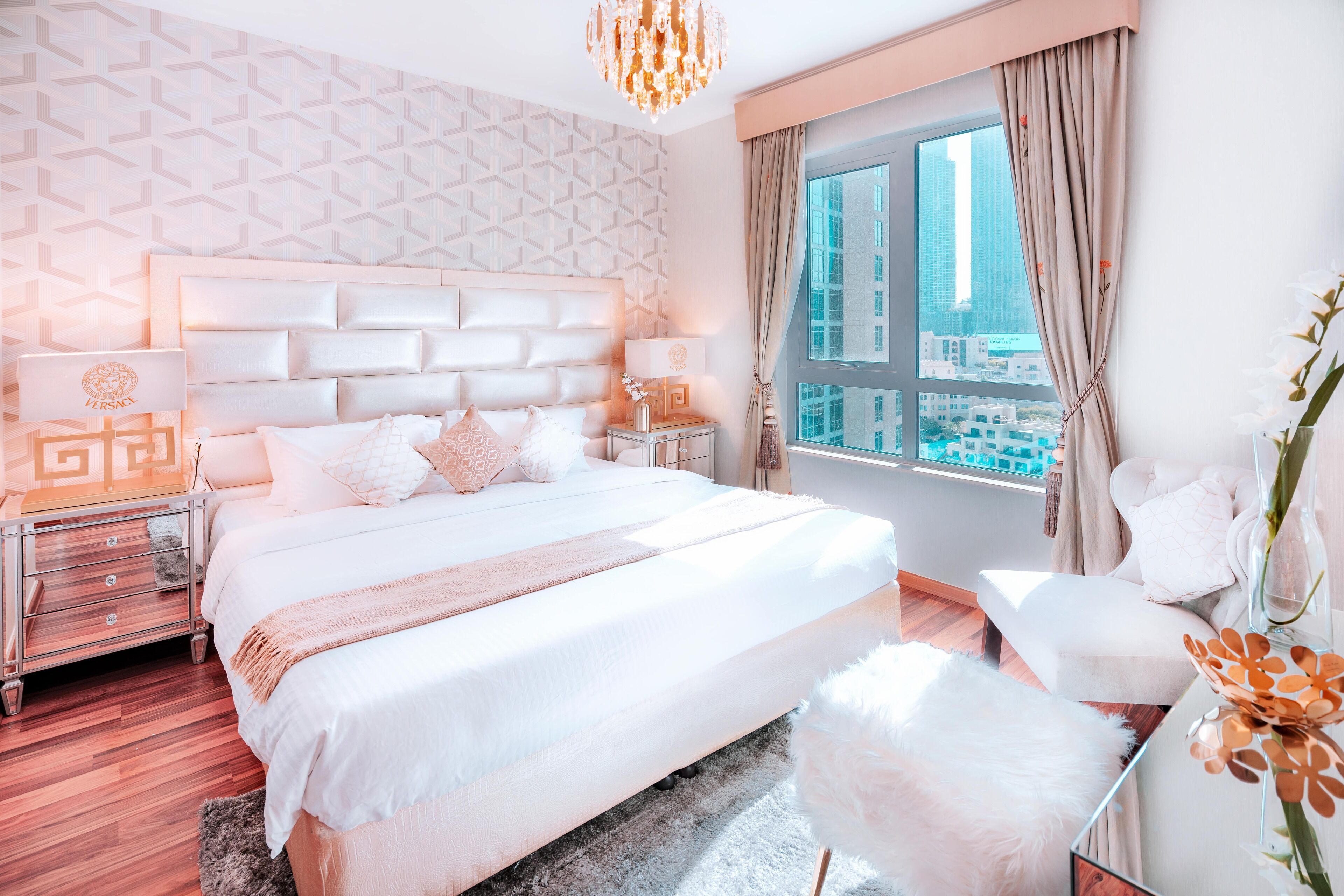 A modern hotel room with a large bed, a city view, and a chandelier.