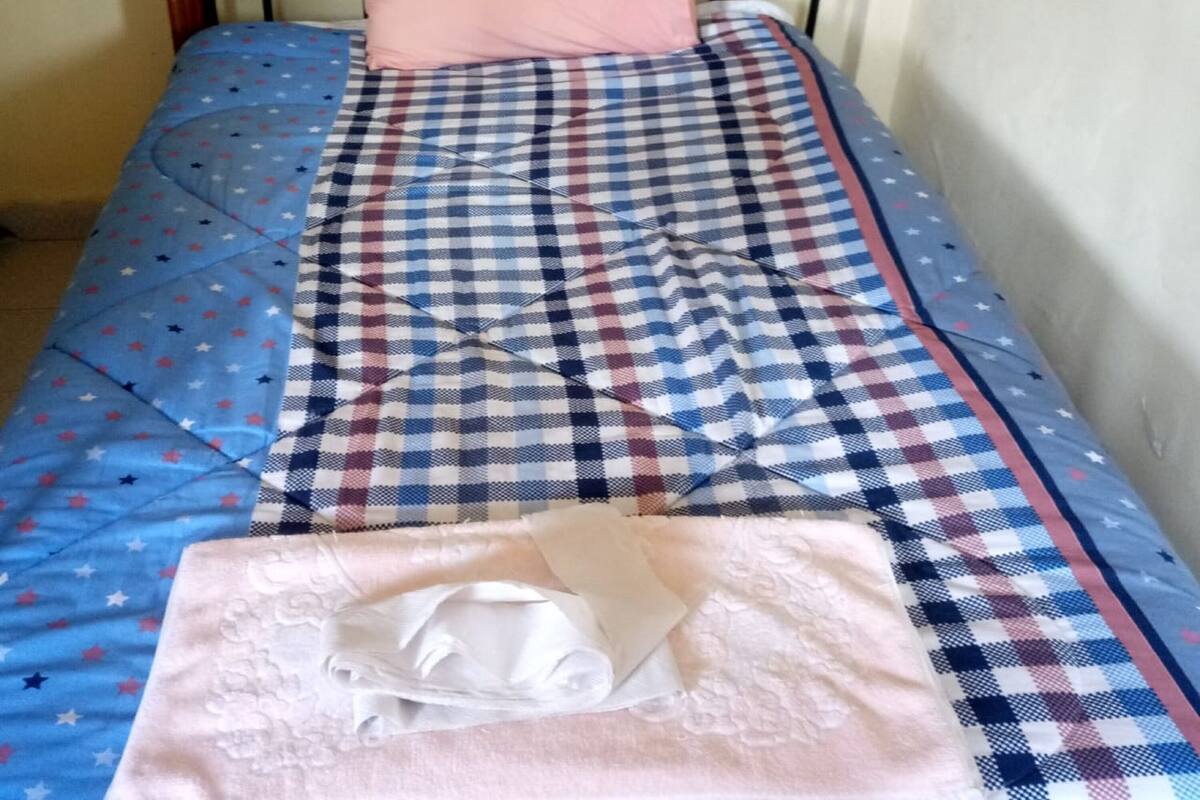 Una cama individual con una colcha de cuadros y una almohada rosa.
