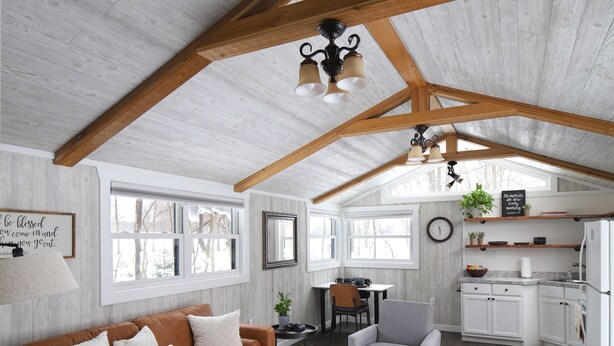 A spacious living area with a high ceiling, wooden beams, a sofa, a coffee table, and a kitchen in the background.