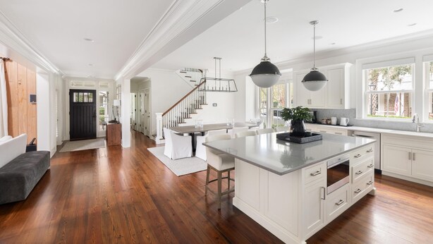 A spacious kitchen with a large island, white cabinetry, and a modern staircase.