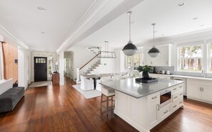 A spacious kitchen with a large island, white cabinetry, and a modern staircase.