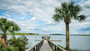A wooden pier leading to a gazebo over water, surrounded by palm trees and greenery.
