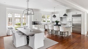 A spacious kitchen with white cabinetry, a central island, and a dining area with white chairs.