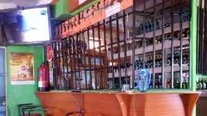 Eine Bar mit Theke, Flaschenregalen, zwei Barhocker und einem Tisch mit einem Plakat.