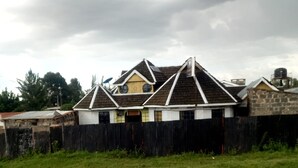 Ein zweistöckiges Haus mit umzäuntem Garten, einer Satellitenschüssel und einem Wassertank auf dem Dach.