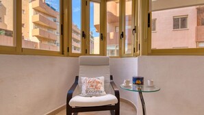 A balcony with a chair, a small table, and a window with a view of neighboring buildings. - Lovely apartment for 4 people with WIFI, A/C, TV and pets allowed (Calpe)