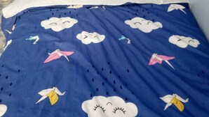 A bed with a blue blanket featuring cloud and origami crane designs, a striped pillow, and a wooden headboard. - Qwetu Guest House (Nakuru)
