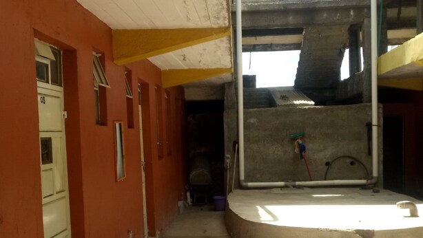 A corridor with a concrete floor, a door labeled "03" on the left, and a window on the right. - Qwetu Guest House (Nakuru)