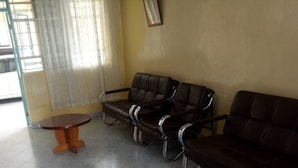 Una habitación con un sofá de cuero marrón, dos mesas de madera y una ventana con cortinas.