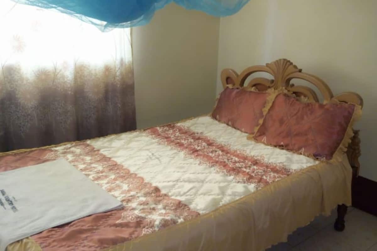 Una cama con una colcha estampada, cabecera de madera y dosel azul.