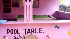 A pool table area with a pink wall, wooden stools, and a sign that reads "POOL TABLE. available." - Sagana Country Hotel (Nyeri)
