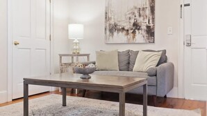 A living room with a grey sofa, a coffee table, a lamp, and a painting on the wall. - Bright & Secluded Apartment with Pool Access (Charleston)
