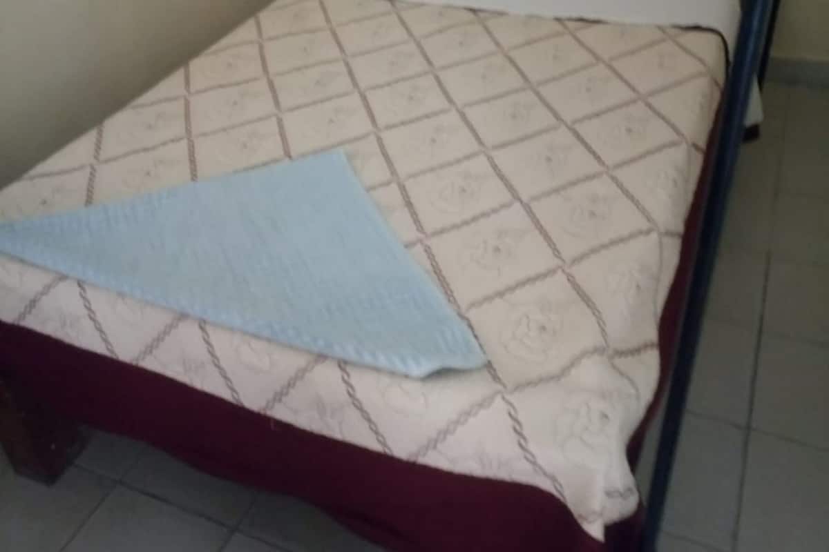A single bed with a quilted mattress, a white pillow, and a blue blanket.