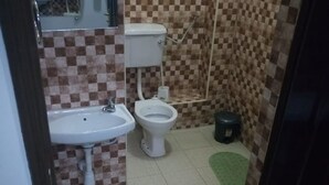 A bathroom with a sink, toilet, and bidet. There are green and red slippers on the floor. - Serena Hotel (Nakuru)