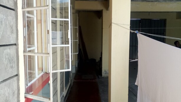 A narrow corridor with a red floor, a window with white frames, and a hanging white cloth. - Serena Hotel (Nakuru)