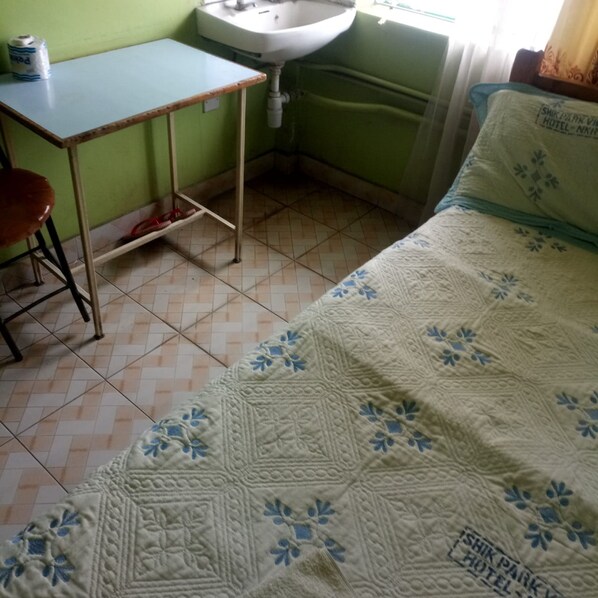 A small, simple room with a bed, a table, a chair, a sink, and a toilet.