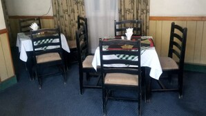 Un comedor con cuatro mesas de madera y sillas, cada una con mantel blanco. El suelo es de alfombra azul y las cortinas tienen un diseño de bambú.