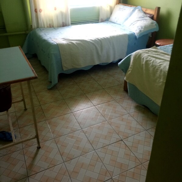 A bedroom with two beds, a small table, and a window with curtains.