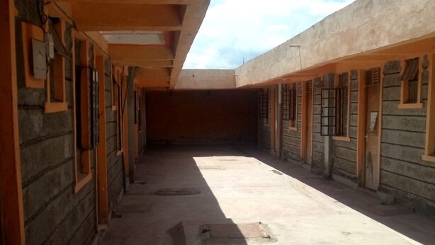 A corridor with stone walls and wooden doors, leading to a courtyard. - Silver Rado West Lodge (Nakuru)