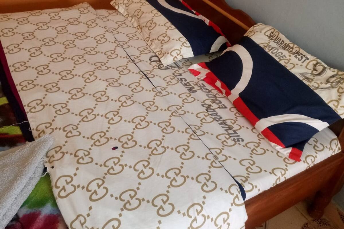 A bed with a patterned bedspread and pillows, a wooden headboard, and a white towel on the floor.