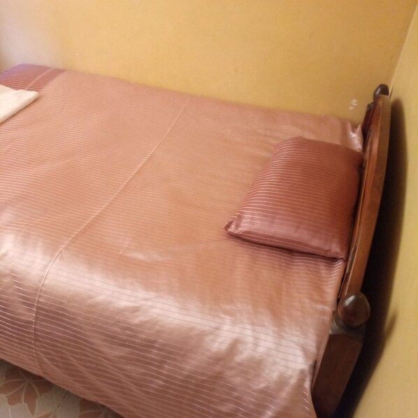 A small, single-bed room with a wooden headboard and a brown striped bedspread.