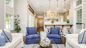 A spacious living room with two blue sofas, a coffee table, and a kitchen in the background.
