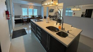 Una cocina moderna con una isla central, doble pileta y una lámpara colgante.