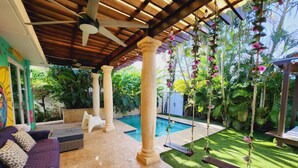Un espacio exterior techado con piscina, asientos y plantas colgantes.