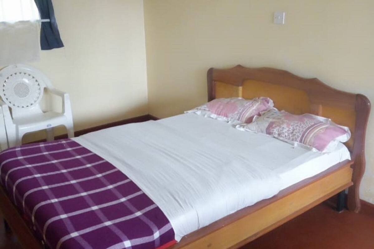 A single bed with a wooden headboard, a white mattress, and a purple checkered blanket.