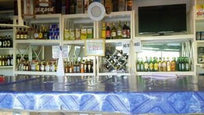 A bar area with a tiled counter, shelves stocked with bottles, a clock, and a television. - Wamagach Kahua- Ini Hotel (Nyeri)