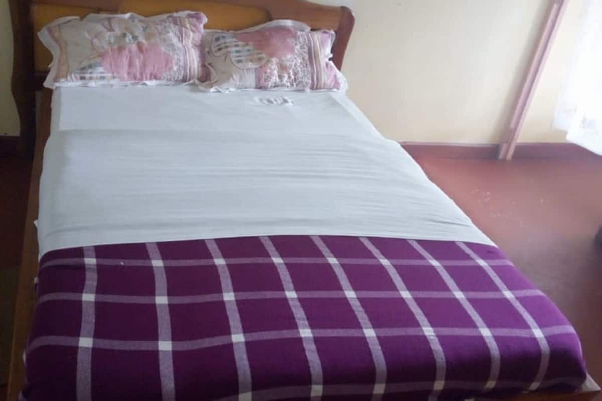 A bed with a wooden headboard, a white mattress, and a purple and white checkered blanket.