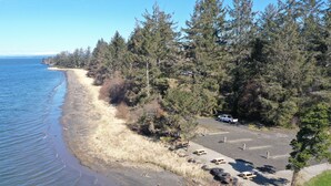 A coastal parking area with a dirt path leading to a beach, surrounded by dense forest and a clear blue sky. - Exclusive Bayside RV Site #4 (Aberdeen)