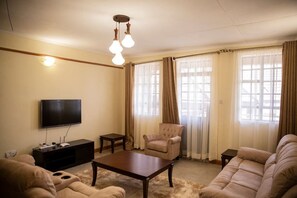 Uma sala de estar com televisão de tela plana, mesa de centro, sofá e uma poltrona.