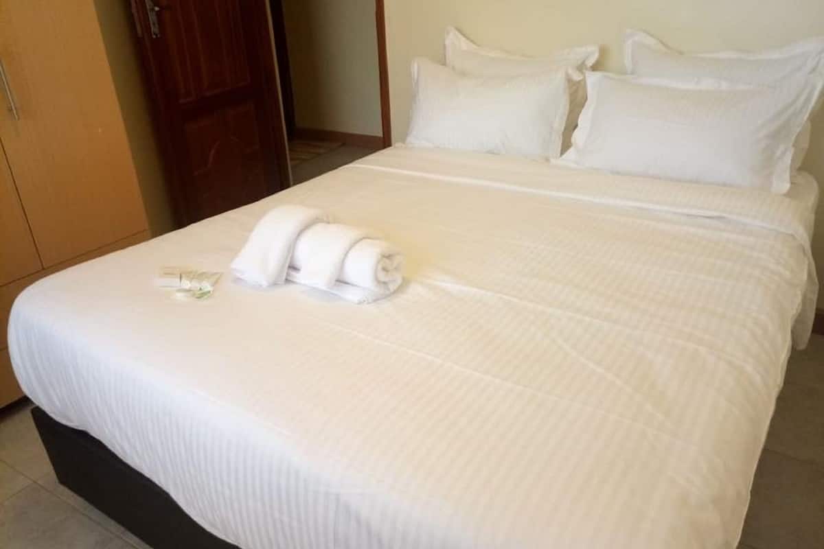 A hotel room with a neatly made bed, a wooden wardrobe, and a door.