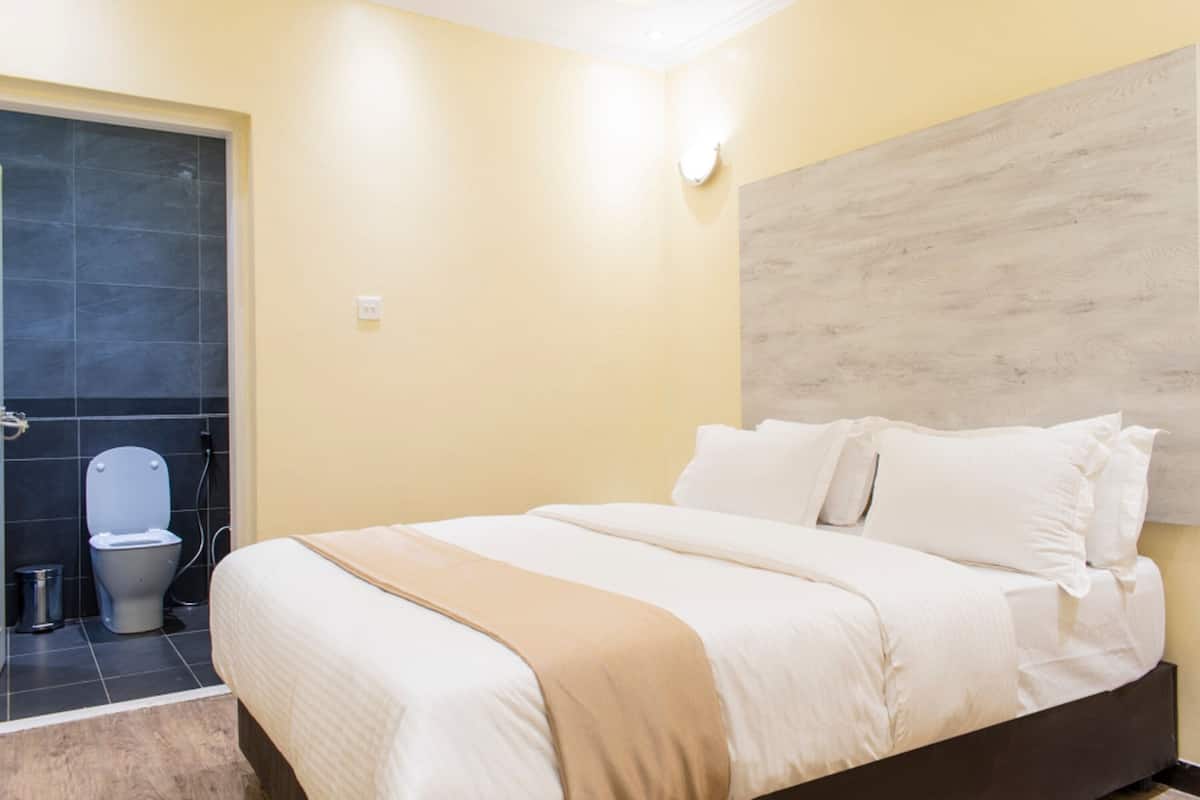 A hotel room with a bed, a bathroom with a toilet and sink, and a shower area.