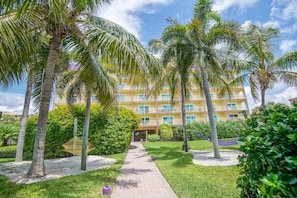 Stroll through lush gardens to the entrance of this tropical retreat, featuring a welcoming pathway and multiple balconies.