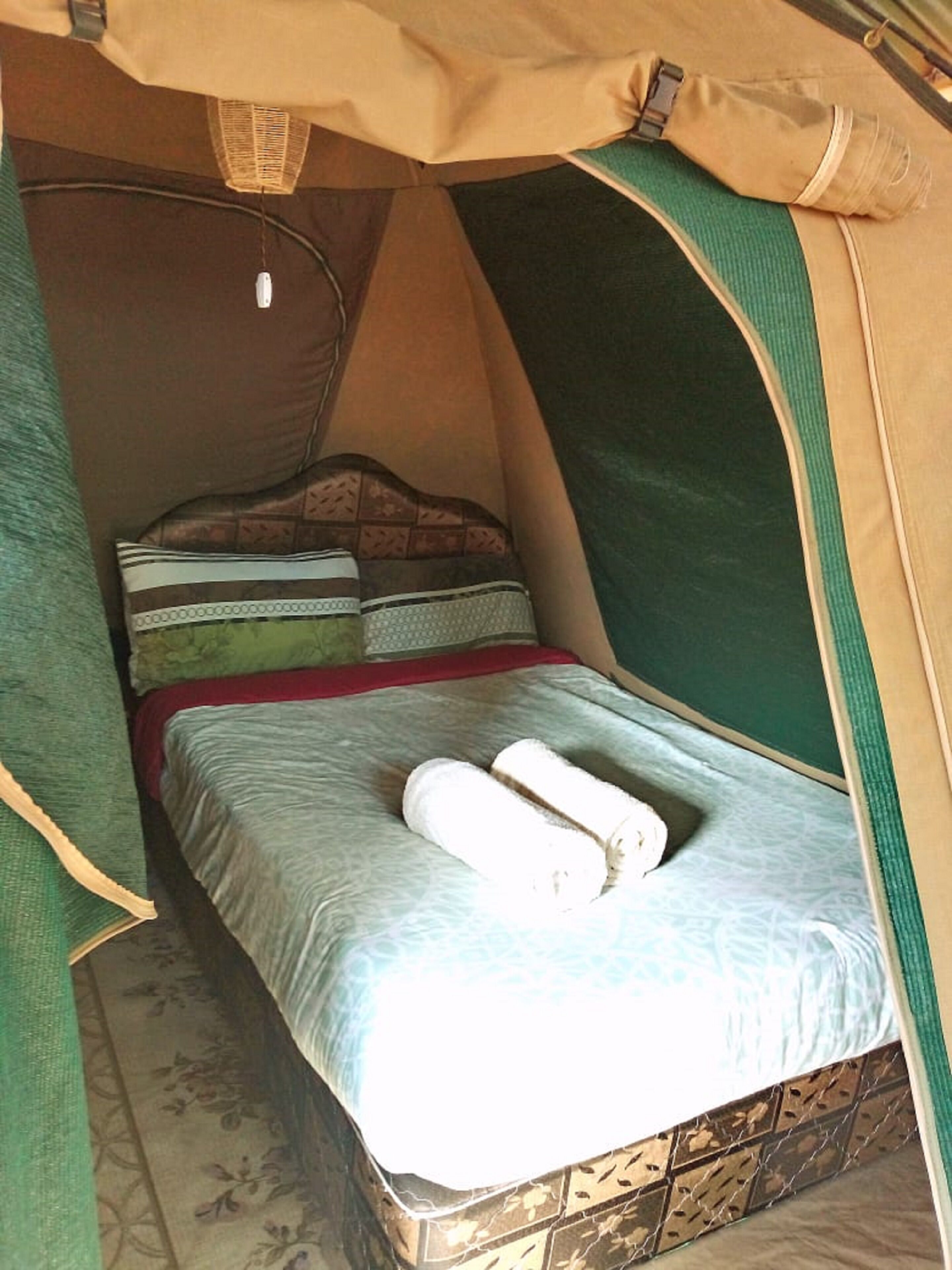 Una tienda de campaña con una cama en su interior, que incluye un colchón, almohadas y una manta enrollada.