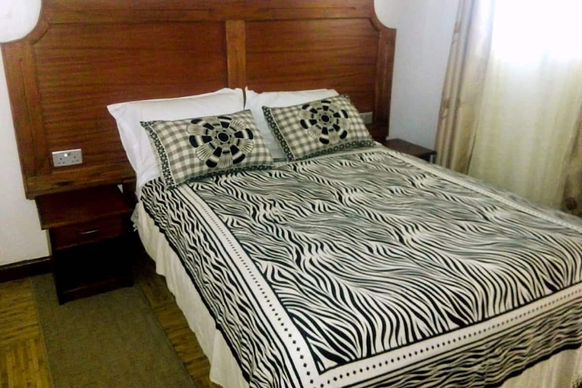 Un dormitorio con cabecera de madera, edredón estampado con diseño de cebra y dos almohadas a cuadros.