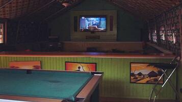 Una habitación con mesa de billar, zona de bar y pantalla de televisión.