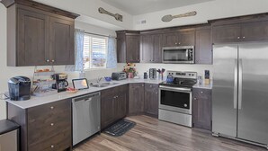 Una cocina moderna con armarios de madera oscura, electrodomésticos de acero inoxidable y un ventanal con cortinas.