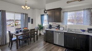 Una cocina moderna con armarios de madera oscura, lavavajillas de acero inoxidable y un comedor con mesa y sillas de madera.