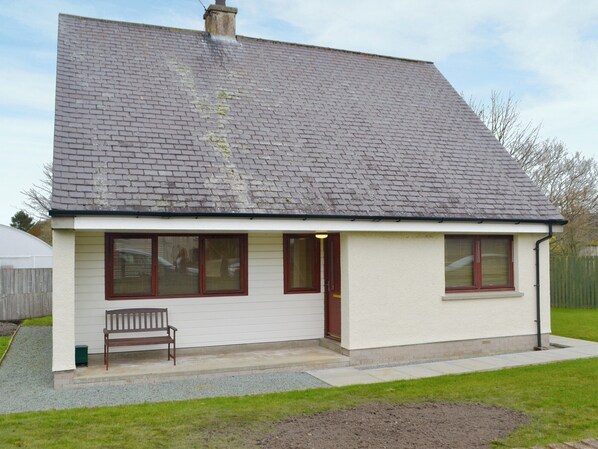 A single-story house with a sloped roof, a front porch with a bench, and a small garden area. - 3 bedroom accommodation in Tain (Tain)