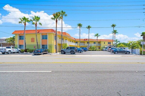 A multi-story hotel with a red roof and yellow walls, parking in front with several cars.