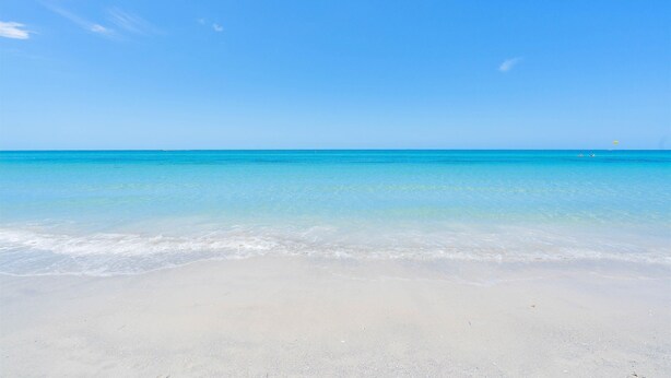 A beach with clear blue water and a sandy shore.
