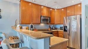 A kitchen with wooden cabinets, a stainless steel refrigerator, a microwave, and a granite countertop.