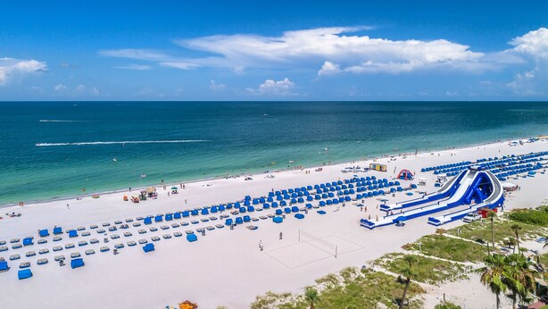 A beach with a water slide and numerous blue lounge chairs. - Cozy Waterfront Condo | Patio & Beach Access (St. Pete Beach)