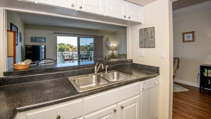 A kitchen with white cabinets, a double sink, and a dishwasher. - Cozy Waterfront Condo | Patio & Beach Access (St. Pete Beach)
