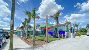 A beachside restaurant with outdoor seating, palm trees, and a no parking sign. - Cozy Waterfront Condo | Patio & Beach Access (St. Pete Beach)